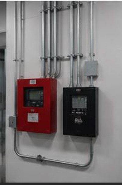 Red and black fire alarm control panels mounted on a wall with conduit above