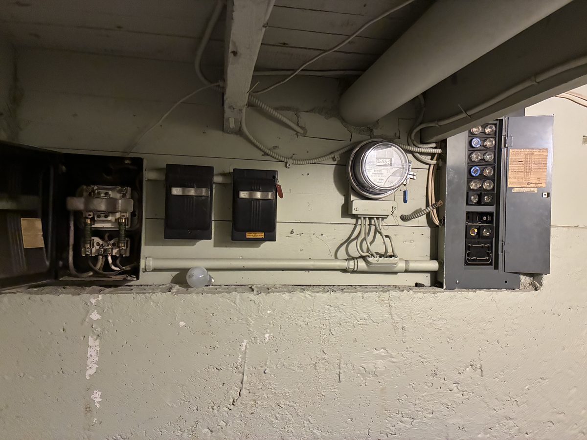 Existing electrical service with meter, fused disconnect and older distribution panel mounted on a basement wall