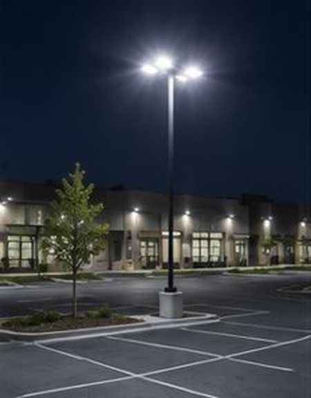 Tall parking lot light pole illuminating a commercial building at night